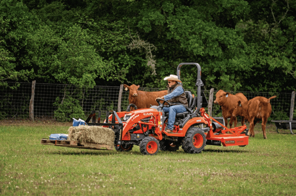 Man using tractor to move pallet of hay stacks