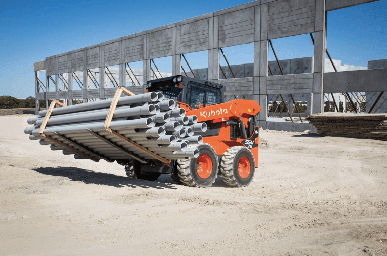 Skid steer moving a stack of pipes