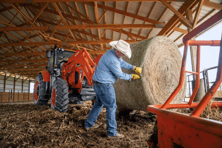 Farmer ripping open hay bale with tractor in the back