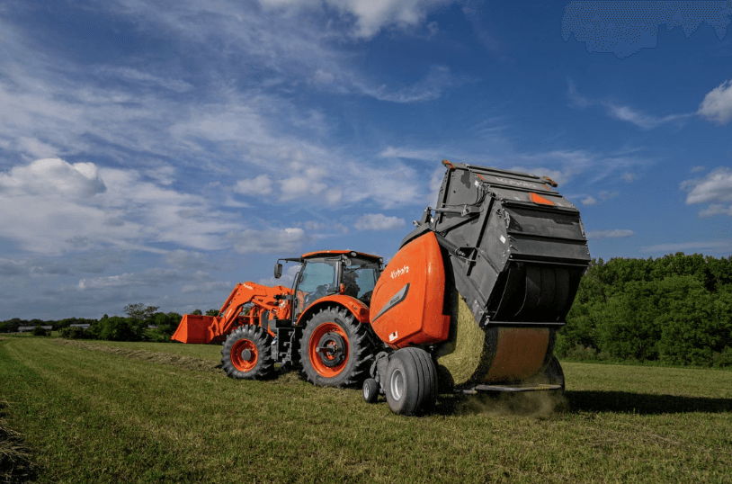 A hay baler hitched to the back of a tractor dumping out hay bale